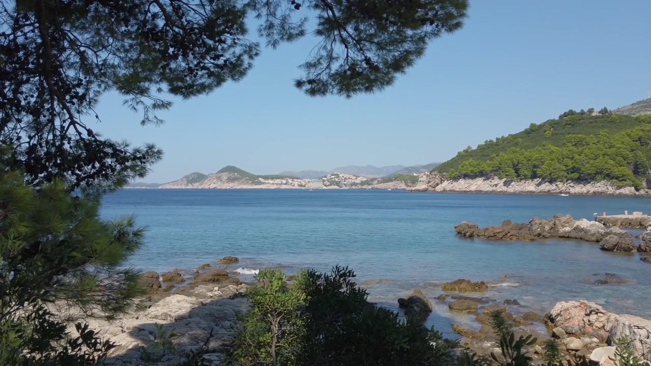 Idyllischer kroatischer Strand mit ruhigem Wasser und entfernten Inseln, umrahmt von üppigem Grün, mediterraner Urlaub