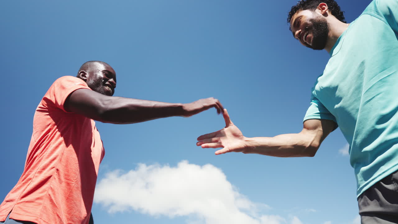 Two Diverse Men Fist Bumping, Shaking Hands, and High Fiving Under Blue Sky