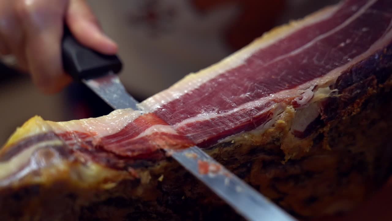 primer plano de la mano de una niña con un cuchillo mientras corta jamón español