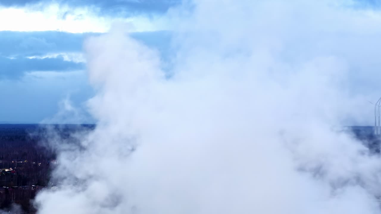 Humo denso o niebla flotando sobre un paisaje invernal, ocultando parcialmente aerogeneradores en la distancia, vista aérea