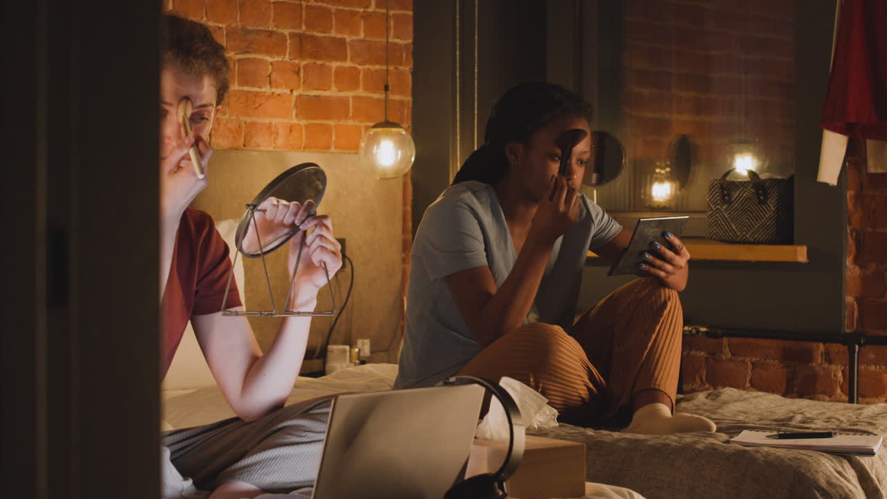 밤에 침실에 있는 침대에서 거울을 사용하여 화장하는 소녀들