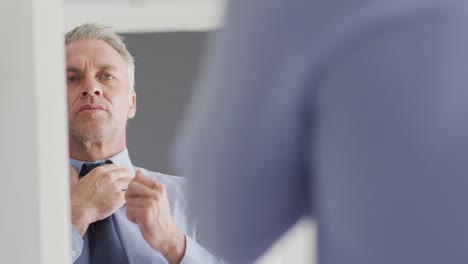 Happy-caucasian-man-looking-at-his-reflection-in-mirror-and-wearing-tie