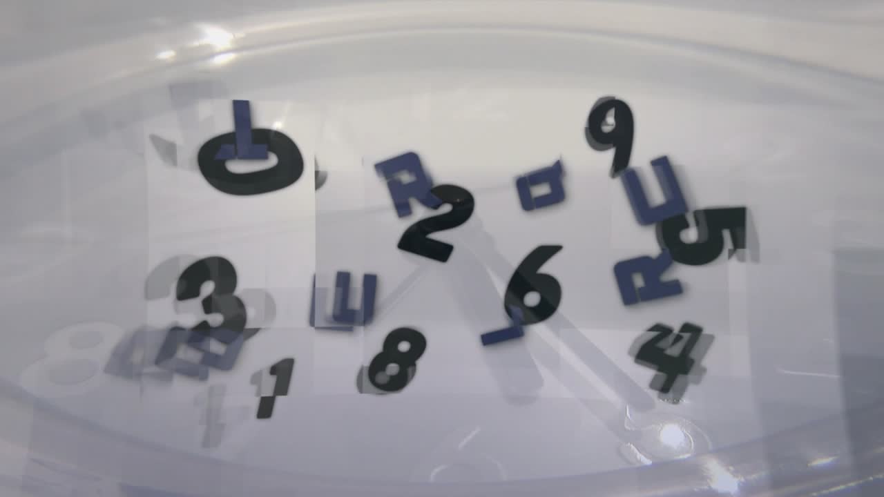 Barretta magnetica che ruota sotto un contenitore, formando un vortice che solleva numeri e lettere per mescolare.