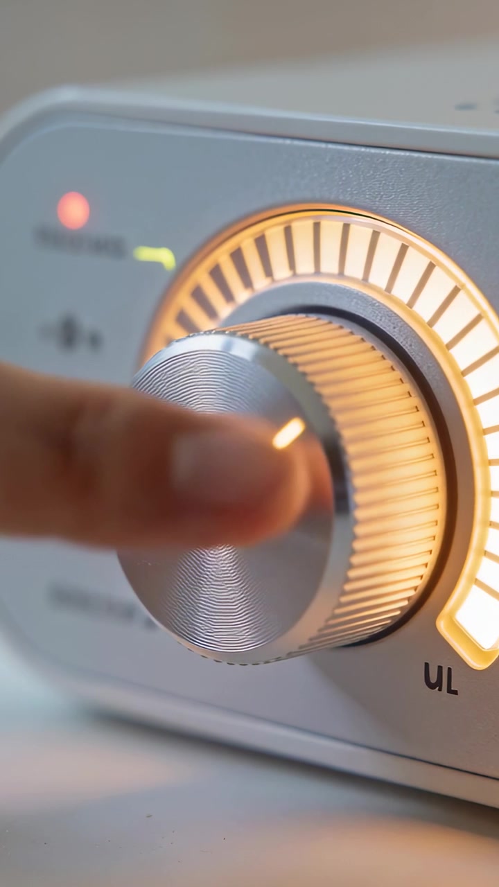Video verticale: Polpastrello che preme e gira una manopola di metallo su un tavolo, illuminando un arco LED per il volume.