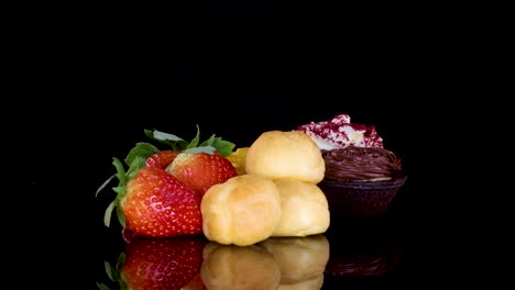 assorted mini desserts, including cupcakes and tarts, rotate on a reflective black surface under lights