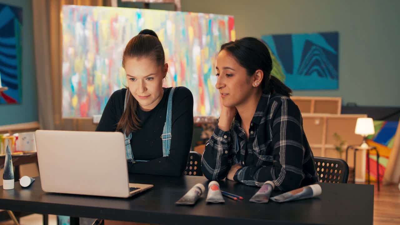 Two great painters, talented artists are working late in studio on laptop, looking for information, preparing project, exhibition of paintings, find sponsors, they are happy, high-five, satisfaction