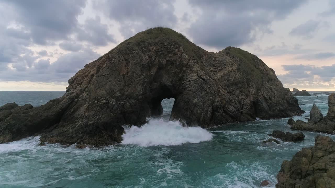 toma cinematográfica aérea de olas que pasan arrojan la cueva de una formación rocosa zipolite, oaxaca