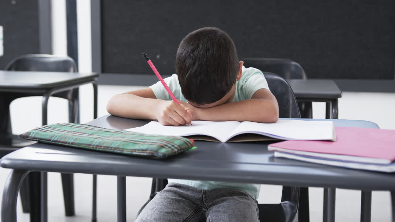 In a school classroom, a young biracial male student rests his head on ...