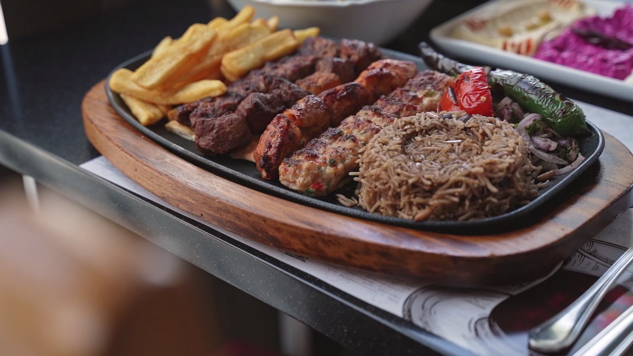 Primo piano di un piatto tradizionale arabo di grigliata mista con spiedini di carne, patatine fritte e riso, servito su un vassoio di legno in un ristorante durante il giorno. Ideale per contenuti culinari e di lifestyle di alta qualità.