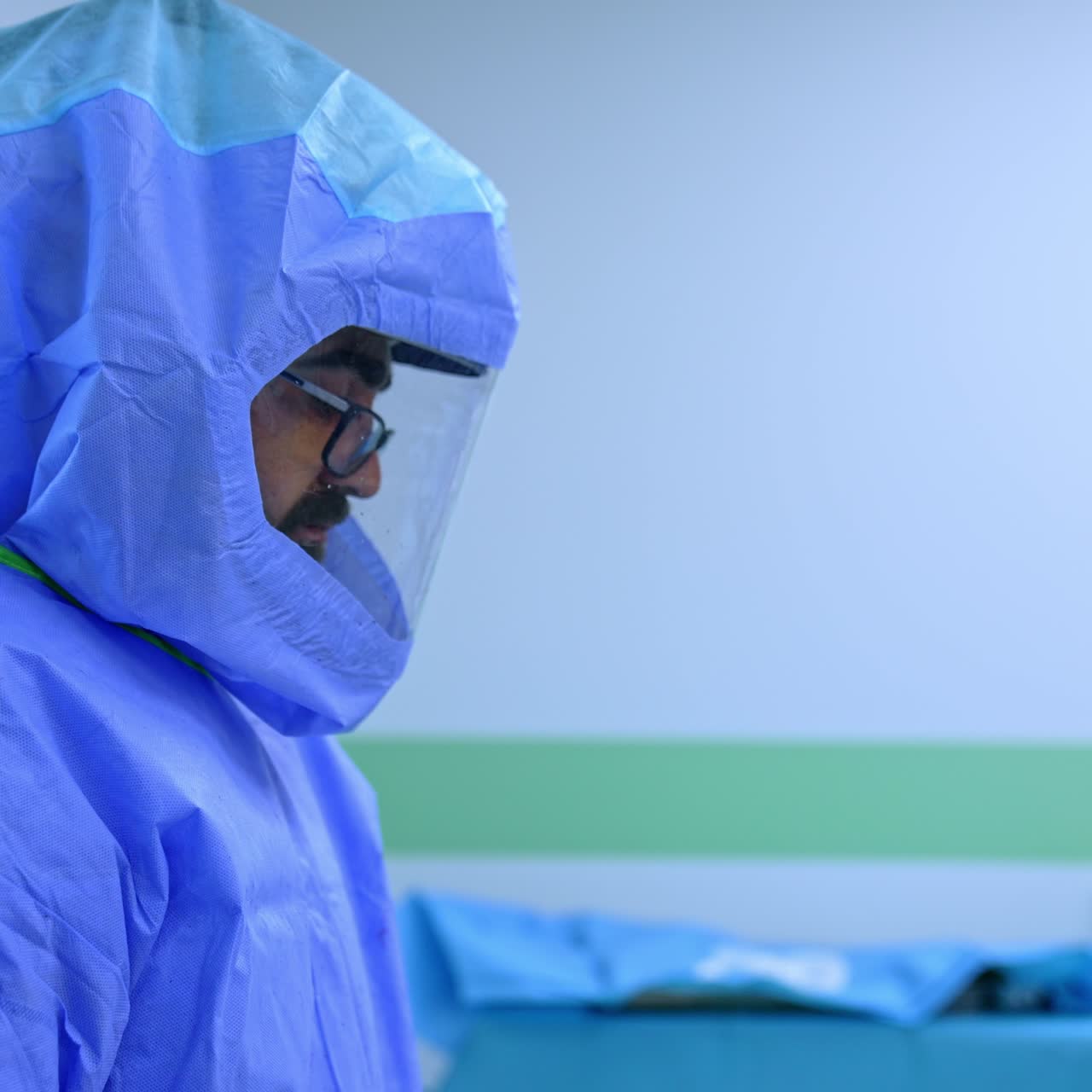 Chirurgo maschio che indossa una tuta medica protettiva e un casco. Ritratto di profilo di un medico in piedi davanti a uno schermo con scansioni di risonanza magnetica.