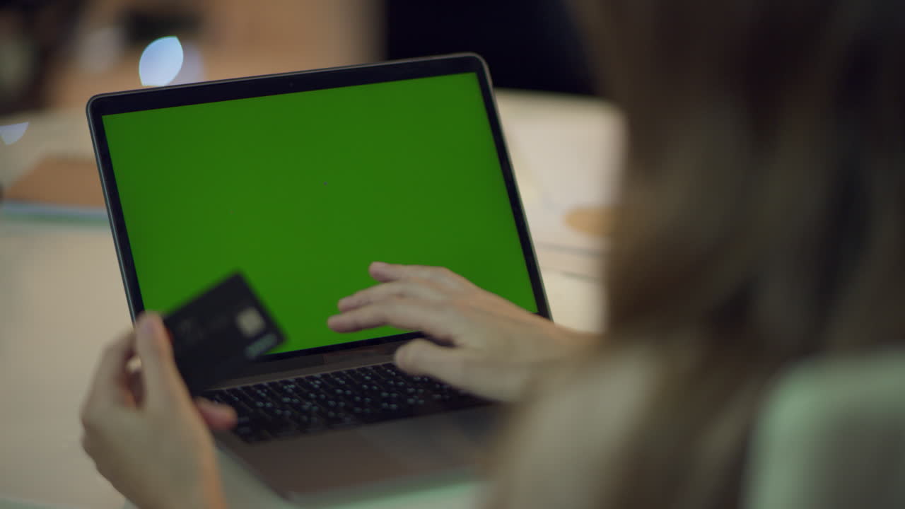 mujer escribiendo datos de tarjeta de crédito en una computadora portátil con pantalla verde