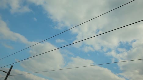 Niedrigwinkelansicht-Eines-Grauen-Masts-Und-Eines-Komplizierten-Netzwerks-Aus-Schwarzen-Stromleitungen,-Die-Sich-Vor-Einem-Leuchtend-Blauen-Himmel-Mit-Weißen-Wolken-Abheben