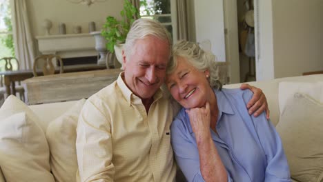 portrait of smiling caucasian senior couple hugging each other while sitting on the couch at home