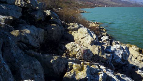 rocks on shore of mountain lake washed by vibrant water on a sunny winter day in the balkans