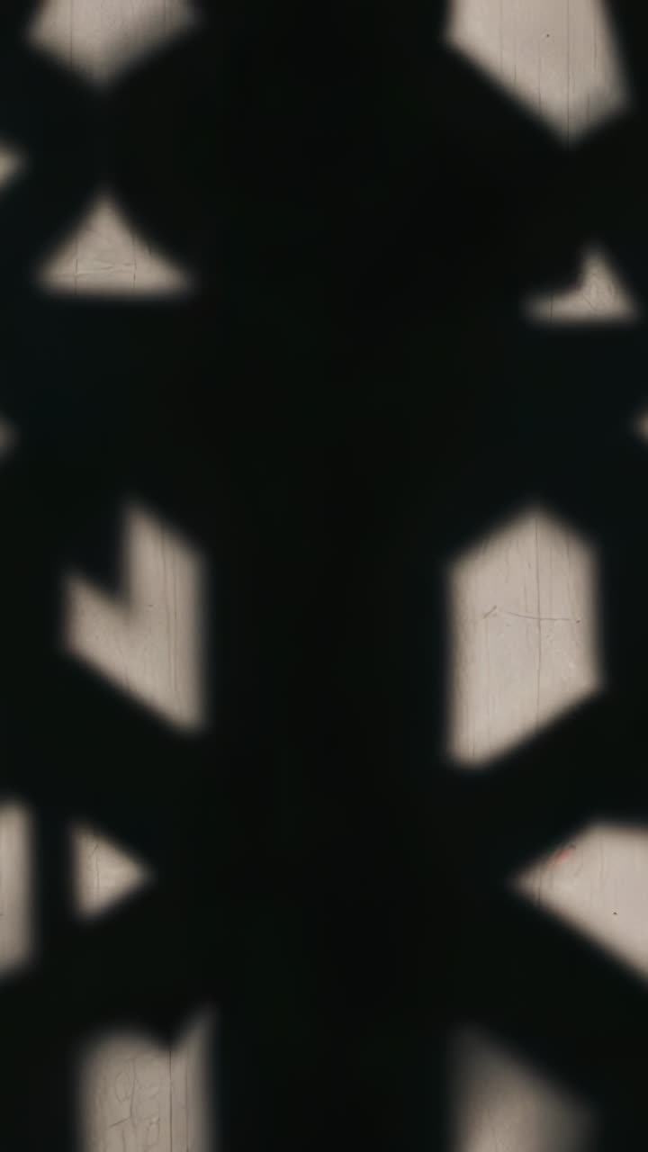 Vertical video: Shifting grille shadow moving across pale drape at window with center band from sun