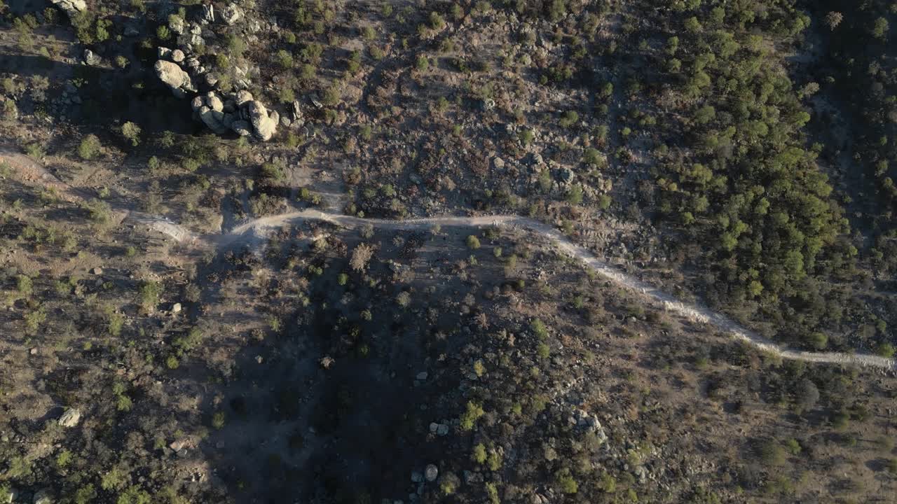 Dry trail cutting through rocky forested terrain in valle de los monjes, aerial view