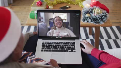 madre y hija afroamericanas usando una computadora portátil para una videollamada de navidad con una mujer en la pantalla