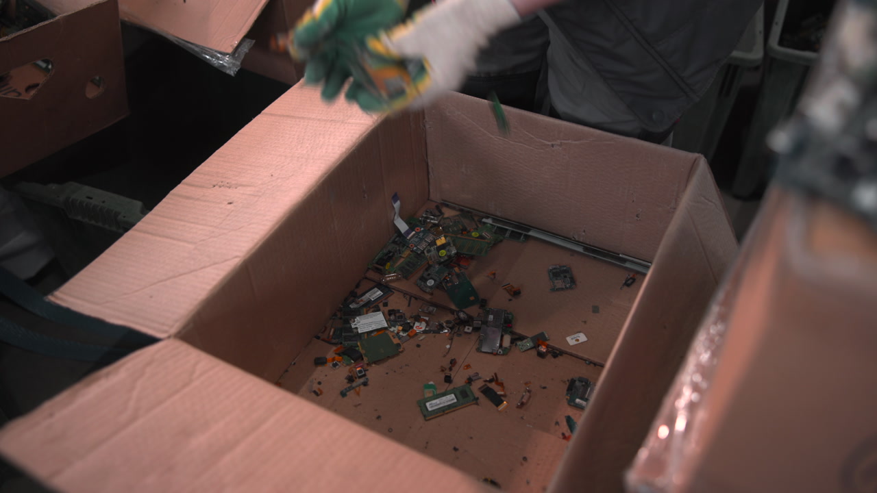 Worker Hands Dropping Circuit Pieces Into Cardboard Box, Gloved Manual Sorting On Packing Line, Close View . Media