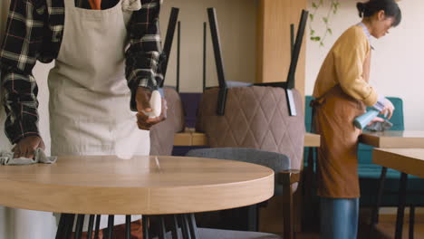 waitress and waiter cleaning coffee shop table with disinfectant spray and rag 2