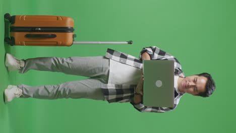cuerpo lleno de viajero masculino asiático con equipaje usando una computadora portátil mientras está de pie en el estudio de fondo de la pantalla verde