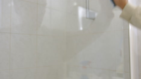 spraying shower glass with cleaner and wiping it, close up