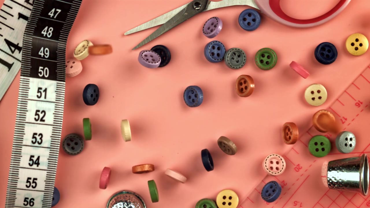Assorted Colorful Buttons Dropping onto a Pink Background with Sewing Supplies