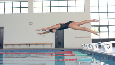 caucasian female swimmer athlete executes a dive at an indoor pool