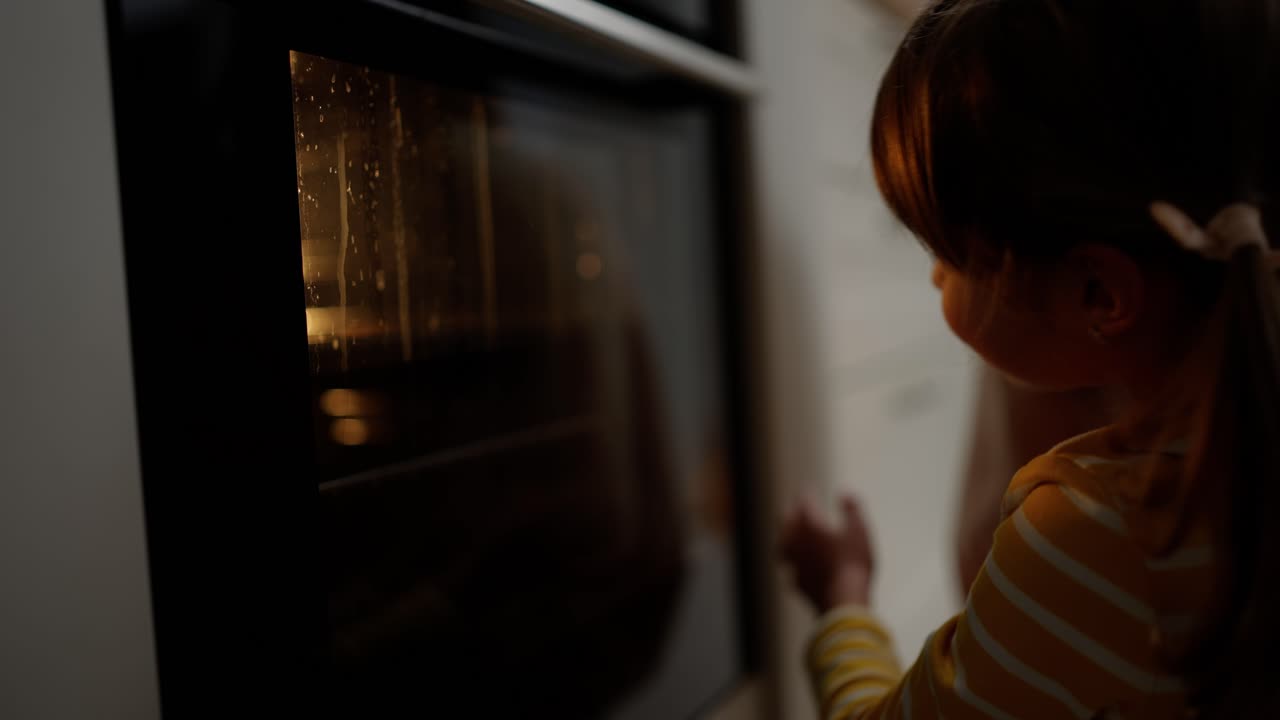 Una bambina guarda attraverso un vetro come i biscotti vengono cotti nel forno.