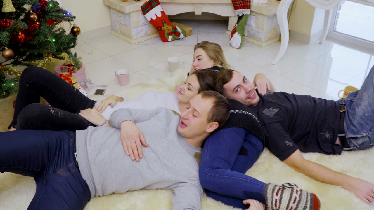 네 명의 젊은 친구들이 크리스마스 트리 근처의 바닥에서 휴식을 취하고 있습니다.
