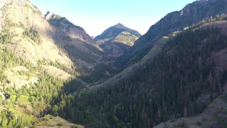 aerial drone reveal of beautiful ouray colorado mountain range and cars driving on highway 550 surrounded by thick pine tree forest and power lines in the rocky mountains