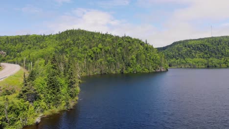 drone footage of a lake as the drone rises up high above the lake with forest-covered mountains in the background and a road with a truck drives on the left