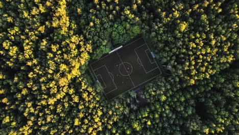 Aerial-screwdriver-shot-above-a-soccer-field-in-middle-of-sunset-lit-forest