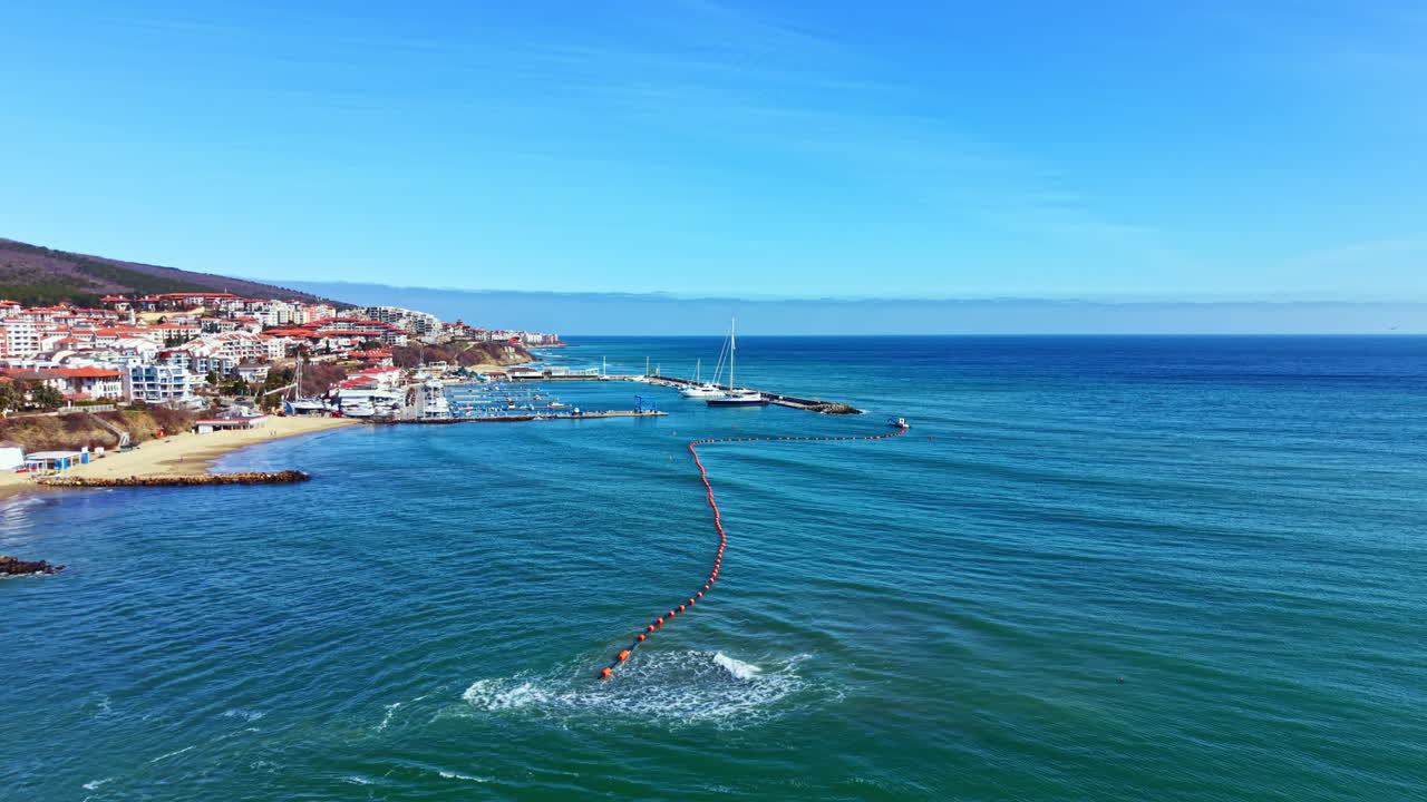 Barche sull'acqua vicino a una spiaggia con edifici sotto un cielo sereno in una località costiera
