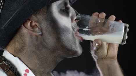 Creepy-man-with-skeleton-makeup-in-white-shirt.-Guy-looking-at-camera,-drinks-milk-from-a-glass