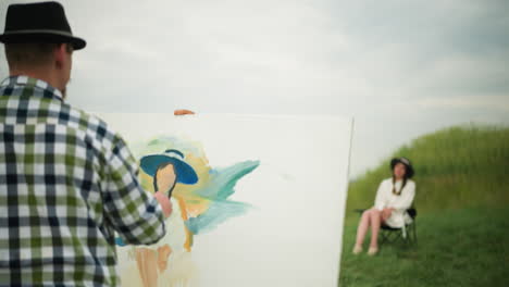 an artist, wearing a hat and a checkered shirt, is focused on painting a portrait on a large canvas while holding a palette. in the background, a blurred woman is seated on a chair in a grass field