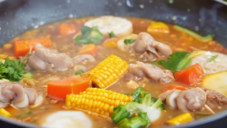 close up of a pot of steaming soup with corn, vegetables, and meat