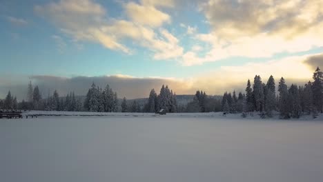 aerial pullback, frozen lake covered with thick snow during winter season in pine forest during dawn dusk, dramatic clouds