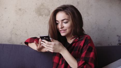 Young-beautiful-brunette-girl-looks-at-her-smartphone-and-acts-surprised.