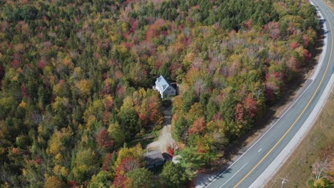 aerial view of freeway and isolated house in colorful forest on sunny autumn day in countryside of new england, maine usa, drone shot