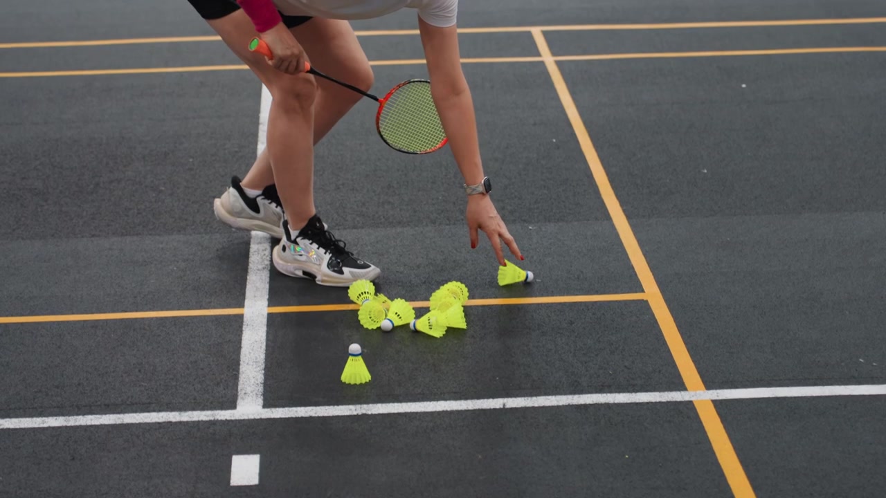 Mujer blanca practicando ejercicios de escalera de bádminton, sesión de juego de pies combinando escalera de agilidad y colocación del volante, entrenando su estado físico para velocidad y coordinación, líneas de la cancha cubierta visibles, rosa.