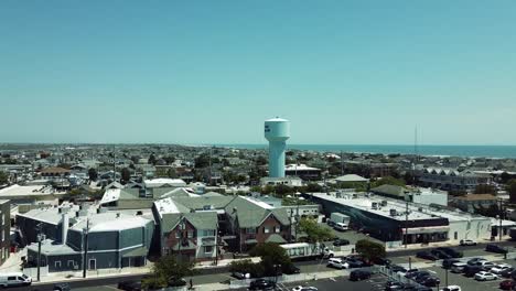 Sobrevuelo-Aéreo-De-Las-Casas-De-Playa-De-Stone-Harbor,-Nueva-Jersey-Con-La-Torre-De-Agua-En-El-Océano-Atlántico-En-El-Horizonte