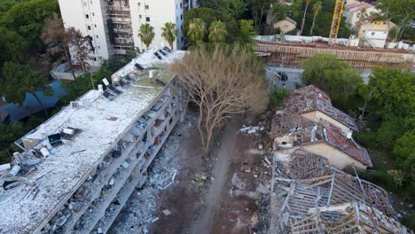 drone circles a tree damaged by an iranian strike in tel aviv, surrounded by two heavily destroyed buildings and widespread debris.