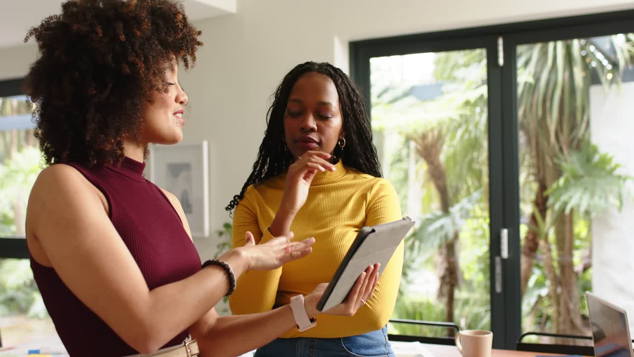 After opening tablet interface Diverse female colleagues at home pointing and tapping tablet screen