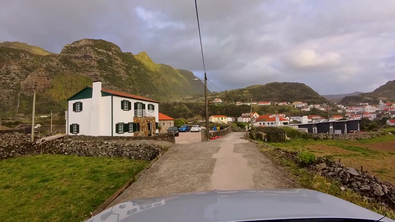 Viaggio panoramico in auto con vista dal veicolo lungo strette strade di villaggio circondate da montagne vulcaniche sull'isola di Flores, Azzorre, Portogallo.