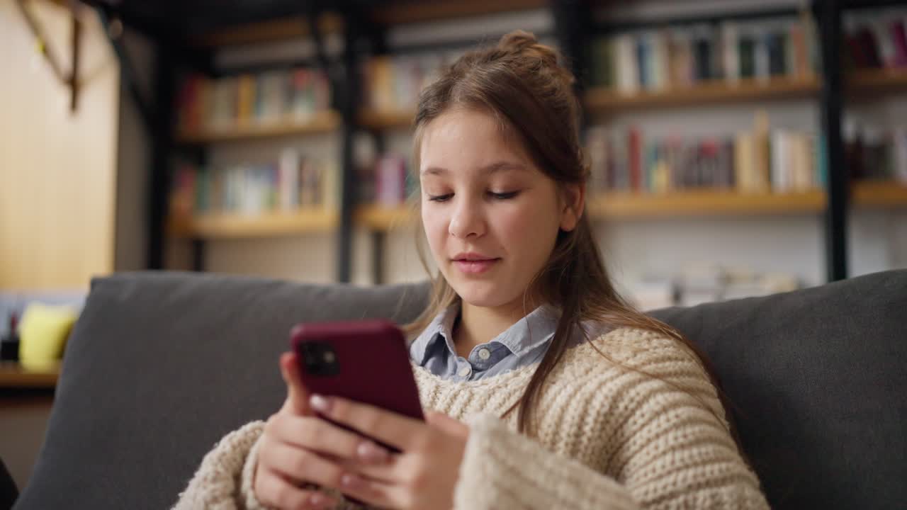 una adolescente usando un teléfono inteligente en un sofá
