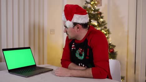 Hombre-De-Negocios-Vestido-De-Manera-Informal-Mirando-Con-Impaciencia-La-Pantalla-Verde-De-Su-Computadora-Portátil-En-La-Oficina-De-Su-Casa-Durante-Las-Vacaciones-De-Navidad-Con-Un-Sombrero-De-Santa