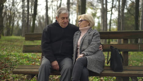 an elderly couple sits together on a bench in the park