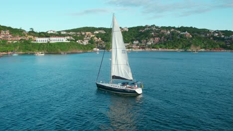 Aerial-view-following-solitary-sailing-ship-navigating-the-shore-of-Joao-Fernandes-beach,-Buzios