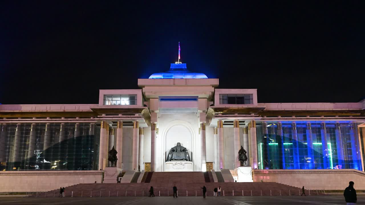 In Ulaanbaatar, a nighttime shot captures people exploring Sukhbaatar Square with the Genghis Khan statue, the Government Palace, and a prominent flag above.