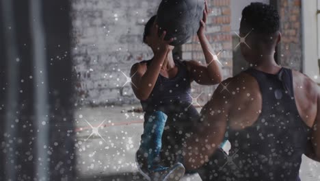 white particles against african american man and woman performing exercise with medicine ball